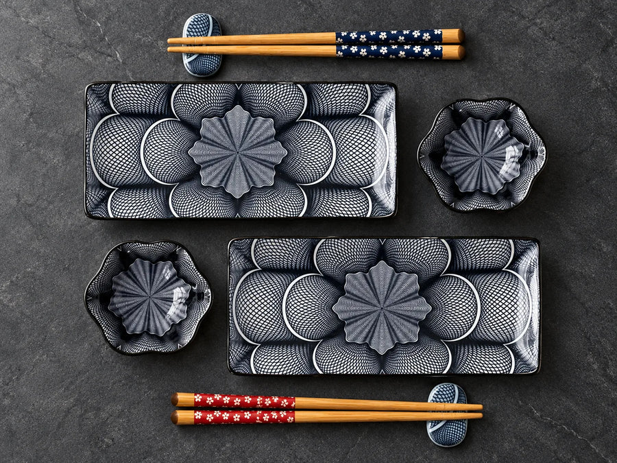 A set of black and gray ceramic tableware with a textured floral pattern, including two rectangular plates, two small bowls, and four pairs of chopsticks with decorative handles, arranged on a dark gray slate surface.