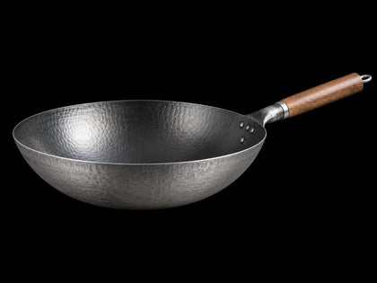 Hammered Japanese wok pan with wooden handle on a black background
