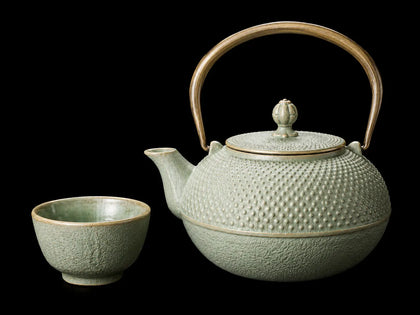 Japanese ceramic teapot and tea cup set with green glaze on a black background
