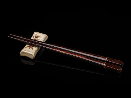 Japanese wooden chopsticks resting on a ceramic chopstick holder on a black background