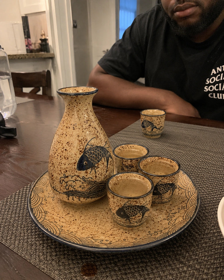 Ceramic sake set with fish design on a table, person sitting in the background